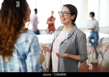 Taille portrait de réussite businesswoman smiling heureusement tout en parlant à collègue in modern office Banque D'Images