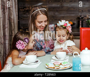 La famille est de boire du thé. Une femme et ses filles sont de boire du thé et de poser dans la cuisine. Avant d'entre eux sont des plaques avec un gâteau fait maison, dans leur ha Banque D'Images