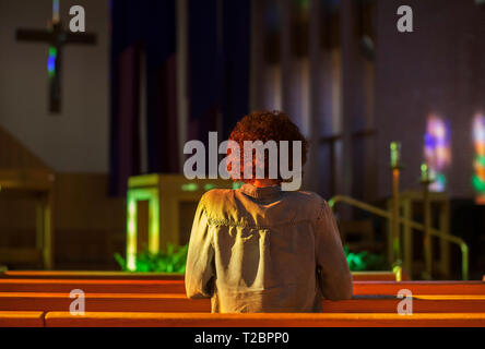 Le vitrail illumine une femme priant dans une église catholique. Banque D'Images