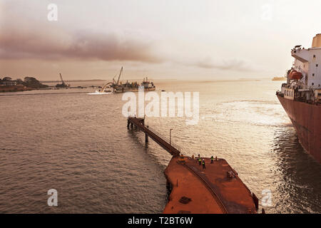 Opérations portuaires pour la gestion et le transport de minerai de fer. Transhipper étant amarré à la jetée pour charger jusqu'à minerai. Drague derrière dredging channel. Banque D'Images