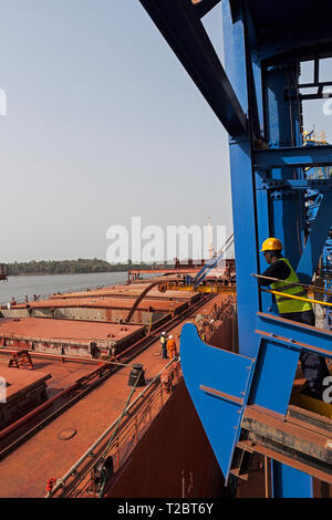 Opérations portuaires pour la gestion et le transport de minerai de fer. Travailleur de chargement d'observation marine bateau transhipper avec ore via chargeurs de navires on jetty Banque D'Images