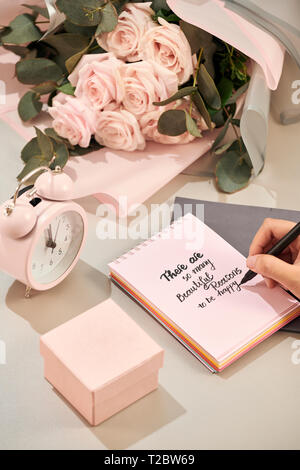 Femme mains tenant un stylo, prêt à écrire. Rose rose, un stylo et une boutique avec coeur rose sur le tableau blanc. Concept d'amour. Saint Valentine's Day concept. Mère' Banque D'Images