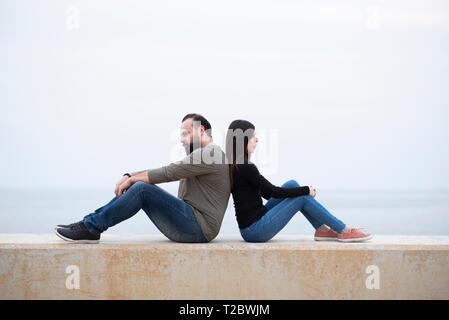 Mand et femme assise dos à dos sur la plage Banque D'Images