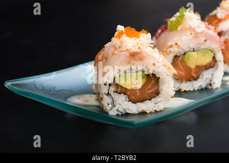 Uramaki spécial, le riz farci au saumon avocat, couverts de sashimi de thon rouge et la mer basse, assaisonné de sauce au fromage, black backgroun Banque D'Images