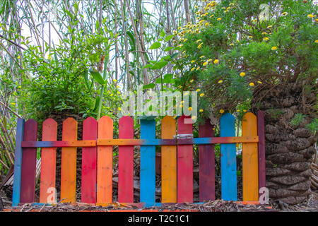 Clôture de couleur multi-bandes et les guichets à l'entrée d'un jardin luxuriant. Vintage Banque D'Images