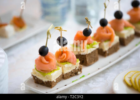 Buffet de plats internationaux.Les canapés sur une assiette blanche. Petits sandwiches sur un bâton. Snack de pain noir, saumon et salade Banque D'Images