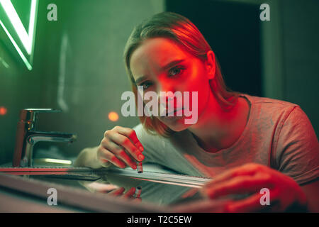 La drogue détruit votre vie. Portrait de jeune drogué avec billet de laminés examine l'appareil photo avant de prendre de la drogue sur la surface de miroir dans le club de nuit Banque D'Images