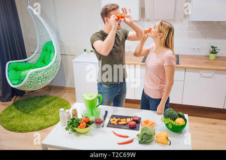 Jeune famille affectueuse a l'amusement avec les tomates biologiques et de piment pendant la cuisson des légumes en cuisine blanche. La nourriture végétarienne. Heureux couple. En bonne santé Banque D'Images