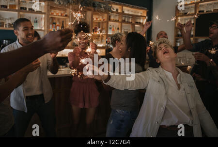 Groupe diversifié de jeunes amis cool clameurs et de célébrer avec les cierges magiques tout en ayant un bon temps dans un bar de nuit Banque D'Images