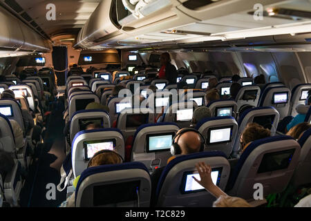 Les passagers assis dans l'avion avion à regarder des films sur des écrans sur le siège avant. Banque D'Images