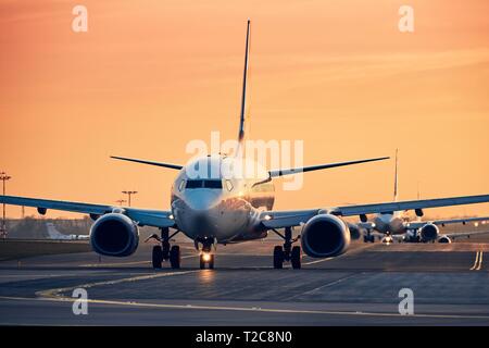 Dans la rangée des avions au sol sur la piste pour décoller. Le trafic à l'aéroport occupé au coucher du soleil. Banque D'Images