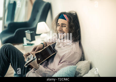 Jeune musicien barbu bizarre faisant des grimaces alors qu'elle repose sur le lit Banque D'Images