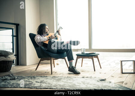 Jeune artiste réfléchie à l'extérieur de la fenêtre tout en se reposant dans un fauteuil Banque D'Images