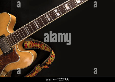 Vintage guitare archtop en érable naturel close-up avec sangle de couleur ci-dessus sur fond noir Banque D'Images