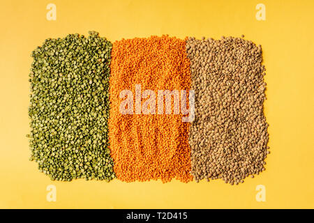 Arrière-plan avec petite orange, jaune et vert lentilles graines de plante légumineuse annuelle, ils sont riches en protéines végétales. Sur fond jaune. Banque D'Images