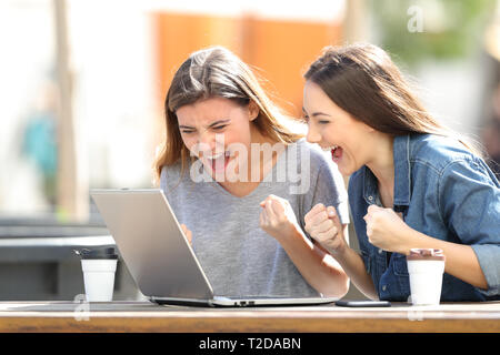 Deux femmes excités contrôler le contenu en ligne ordinateur portable assis dans un parc Banque D'Images
