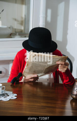 Vêtus de noir coloré mini hat grey haired woman fantaisie avec de la canne à sucre est la lecture d'un très vieux magazine papier miteux usé étroitement à face à dinn Banque D'Images