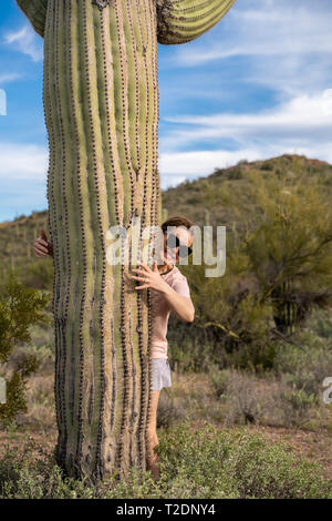 Mignon femelle femme se tient à côté d'un grand cactus Saguaro dans le désert de Sonora, en lui donnant une accolade avec ses bras Banque D'Images