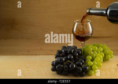 Deux grappes de raisin, noir et blanc, et un verre de vin rouge sur un fond de bois, éclairage de studio, vue du dessus Banque D'Images