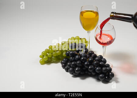 Deux grappes de raisins blancs et noirs et des verres de vin sur un fond blanc, éclairage studio Banque D'Images