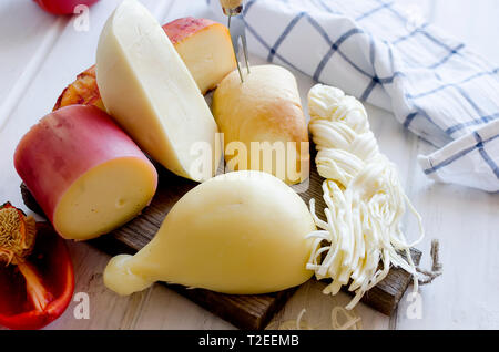 Assortiment de fromages faits maison dans diverses formes et tailles sur le fond de bois, suluguni, cochon, Cacocavallo avec tomates et fines herbes Banque D'Images