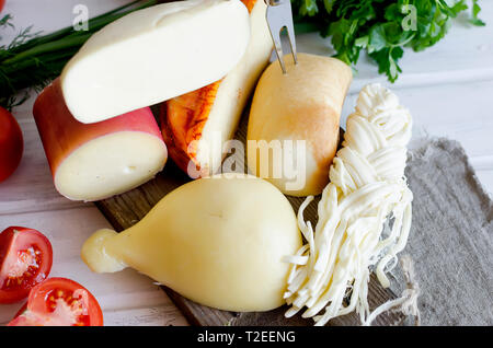 Assortiment de fromages faits maison dans diverses formes et tailles sur le fond de bois, suluguni, cochon, Cacocavallo avec tomates et fines herbes Banque D'Images