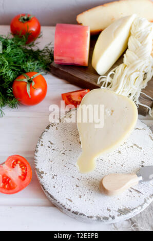 Assortiment de fromages faits maison dans diverses formes et tailles sur le fond de bois, suluguni, cochon, Cacocavallo avec tomates et fines herbes Banque D'Images