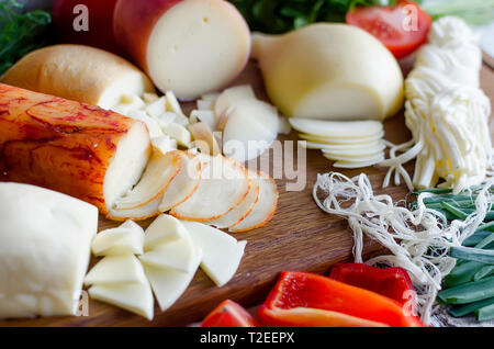 Assortiment de fromages faits maison dans diverses formes et tailles sur le fond de bois, suluguni, cochon, Cacocavallo avec tomates et fines herbes Banque D'Images