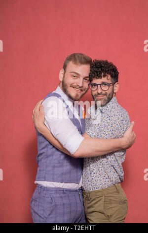 Deux hommes, gay couple hugging and posing in studio, à la recherche d'appareil photo. fond rose derrière. Banque D'Images