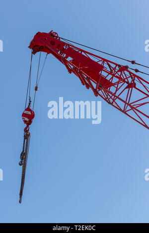 Haut de la grue rouge avec le crochet et les chaînes de levage contre ciel bleu clair Banque D'Images