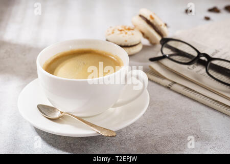 Tasse de café avec ses macarons français, journal et lunettes dans l'arrière-plan. Le petit-déjeuner gratuit. Banque D'Images