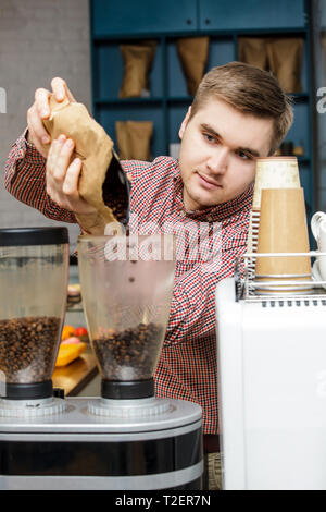 Un jeune homme en chemise à carreaux verse de grains de café dans une machine à café. Café Barista ajoute à la rectifieuse de café. Banque D'Images