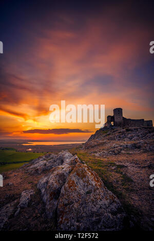 Ancienne citadelle en ruine sur une colline rocheuse située dans le comté de Constanta en Roumanie appelé Enisala tourné au coucher du soleil avec quelques rochers dans l'avant-plan et d'un lac je Banque D'Images