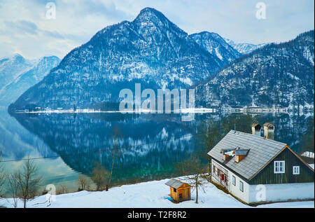 Vieille maison traditionnelle sur la banque de neige Hallstattersee lake avec vue sur le mont Lockerkogel, réfléchissant sur la surface de l'eau miroir, Bad Goisern, Banque D'Images