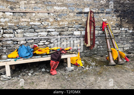 Robe de moine bouddhiste accroché sur un mur à côté de deux dungchens tibétains (cornes), des moines bouddhistes tibétains et de cymbales jaune, Tengboche, Népal Banque D'Images