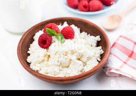 Bol de fromage cottage, tvorog ou fromage blanc avec des framboises fraîches sur tableau blanc. Riche en calcium des produits laitiers sains Banque D'Images