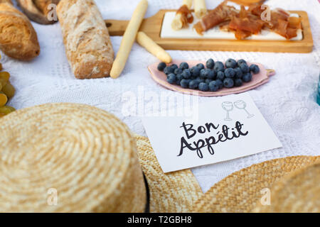Les chapeaux de paille se coucha sur une couverture de pique-nique blanc à côté de plaque constructeur bon appétit journée d'été lumineux arrière-plan. Semaine de l'été les loisirs. Banque D'Images