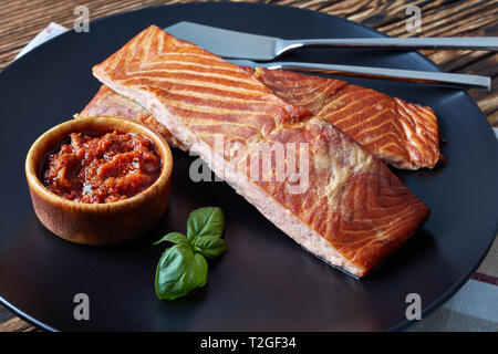 Filet de saumon au four sur une plaque noire avec sauce tomates séchées au soleil sur une vieille table en bois, vue horizontale à partir de ci-dessus, close-up Banque D'Images