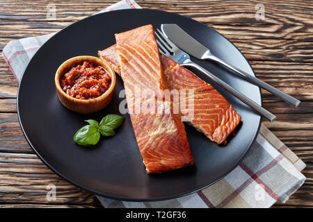 Filet de saumon au four sur une plaque noire avec sauce tomates séchées au soleil sur une vieille table en bois Banque D'Images