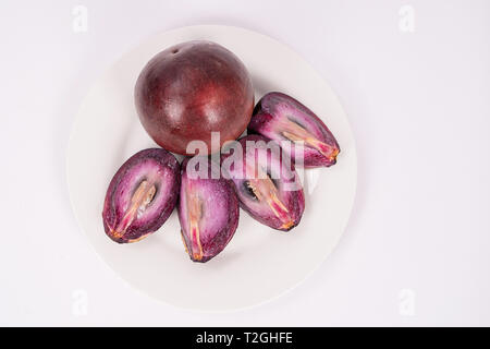 Deux fruits caimito sur une plaque, l'un d'entre eux réduit de quatre pièces Banque D'Images