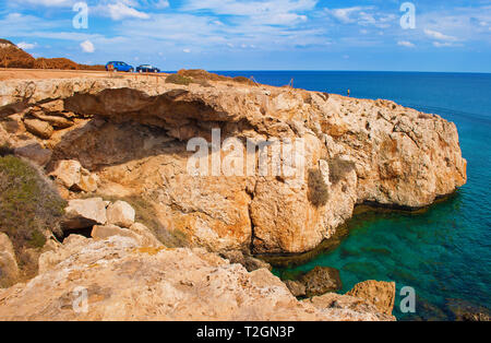 Une petite figure d'homme debout sur le bord d'une falaise. Deux voitures près d'une baie près de Cape Greco, Chypre. La côte près de deep green Rock azure transparent Banque D'Images