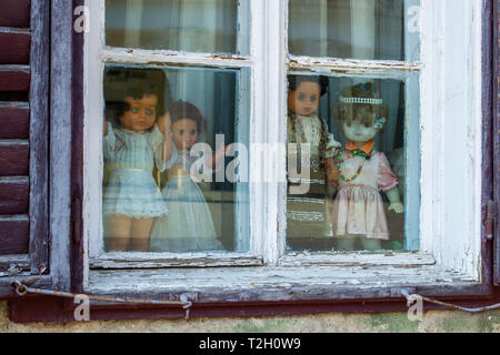 Quatre poupées creepy vêtu de blanc et avec des vêtements traditionnels roumains, affichées dans une fenêtre, en regardant les gens passer. Close up of p Banque D'Images