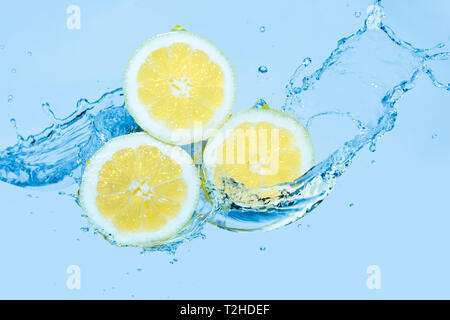 Les éclaboussures d'eau sur des tranches de citron contre un fond bleu clair Banque D'Images