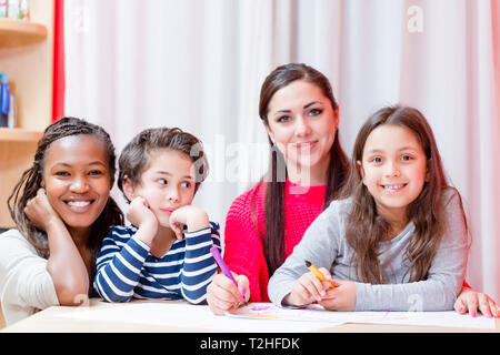 Portrait of smiling woman sitting avec enfants faire le dessin sur table Banque D'Images