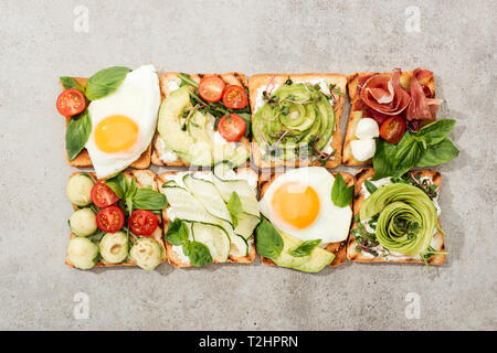 Vue de dessus de toasts avec des légumes, œufs frits et de prosciutto sur la surface texturée Banque D'Images