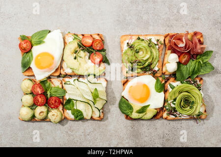 Vue de dessus de toasts avec des légumes, œufs frits et de prosciutto sur la surface texturée Banque D'Images
