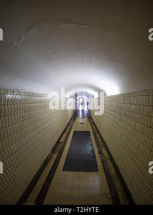 Un long tunnel piétonnier souterrain avec la lumière à la fin. Silhouettes de personnes sont visibles à l'avant. Banque D'Images