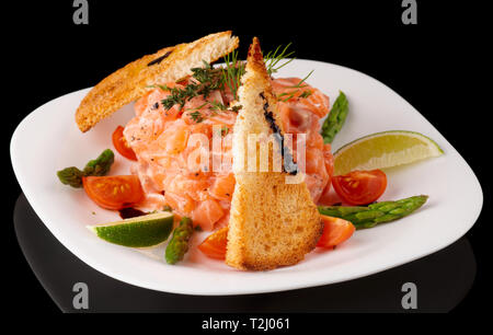 Carpaccio de saumon avec des croûtons et des légumes dans la plaque isolé sur fond noir Banque D'Images