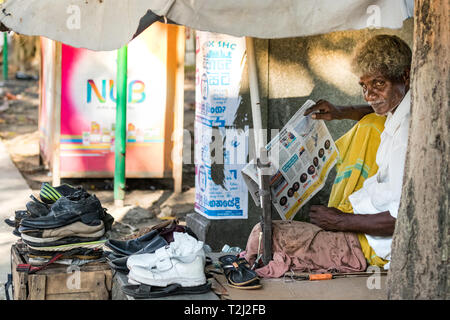 Galle, Sri Lanka - Février 18th, 2019 : Portrait of a senior man holding a Sri Lanka, la page de journal à vendre des chaussures assis dans la rue dans la vésicule Banque D'Images