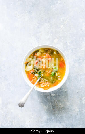 Minestrone, sur la Cuvette et pot de légumes couper sur une cutboard tomate cerise, citron vert, brun sur un fond blanc en béton Banque D'Images